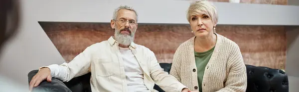 Уважна пара середнього віку сидить на шкіряному дивані і дивиться на психолога, банер — стокове фото