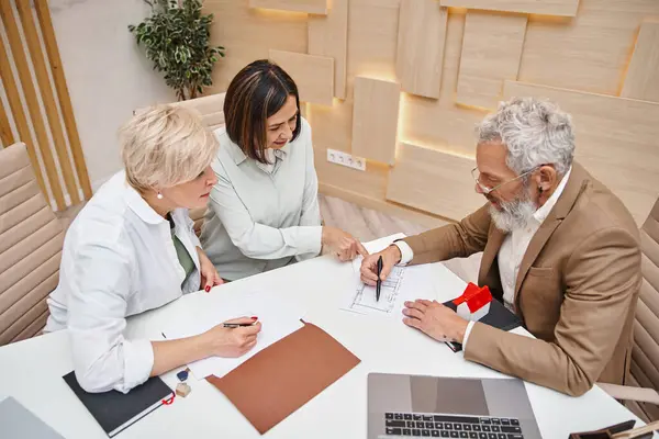 Realtor showing blueprint of apartment to middle aged interracial lgbt couple in real estate office — Stock Photo
