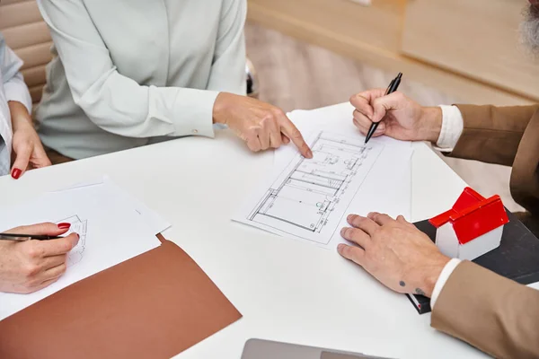Cropped woman pointing at blueprint of new house near realtor in real estate office, lgbt couple — Stock Photo