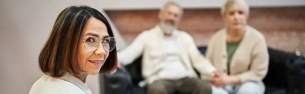 Bannière, psychologue d'âge moyen dans des lunettes regardant la caméra près du couple marié sur toile de fond — Photo de stock