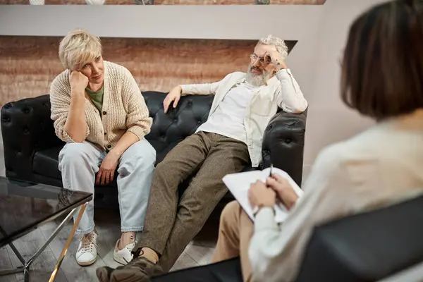 Tired married couple sitting on leather couch during family consultation near psychologist — Stock Photo