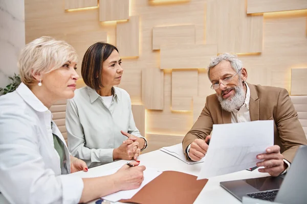 Bearded realtor holding contract near lesbian couple in real estate office, middle aged lgbt family — Stock Photo