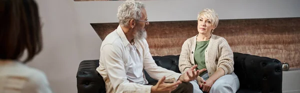Бородатий чоловік розмовляє з дружиною середнього віку поблизу психолога під час сеансу терапії, банер — стокове фото