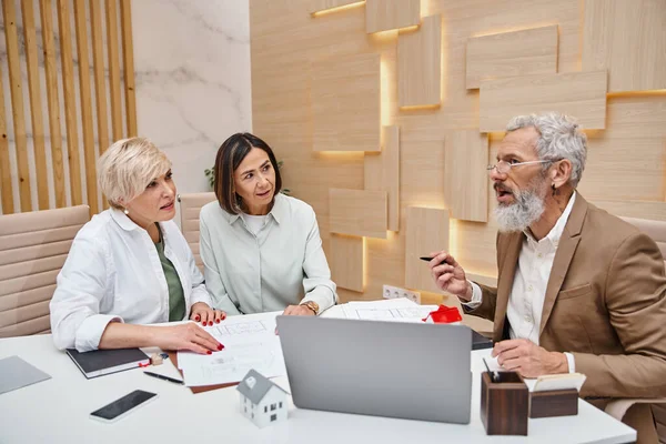 Middled aged and tattooed realtor discussing purchase of real estate property with lesbian couple — Stock Photo