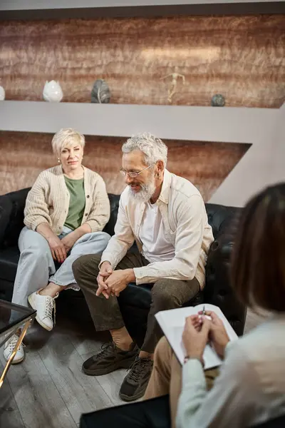 Подружня пара середнього віку сидить на дивані і обговорює проблему біля психолога під час сеансу — стокове фото