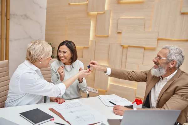 Tattooed realtor giving key from new house to joyful middle aged lgbt couple, real estate purchase — Stock Photo
