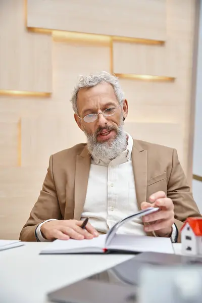 Middle aged real estate agent in glasses talking during consultation, checking his notes in office — Stock Photo
