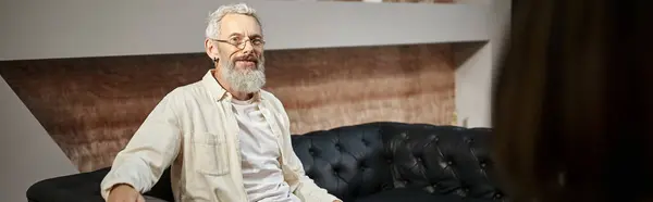 Happy middled aged man with tattoo sitting on leather couch and looking at psychologist, banner — Stock Photo
