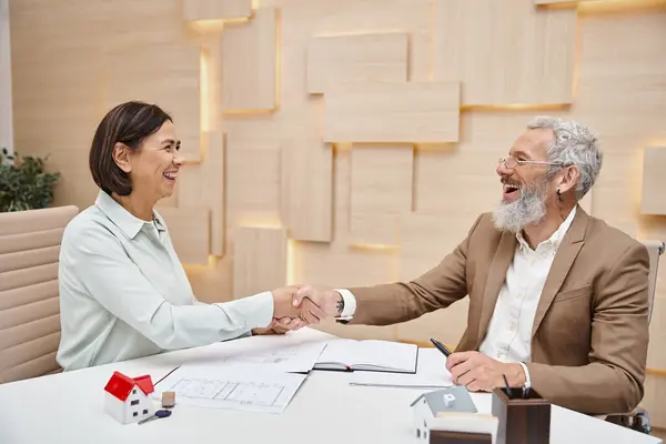 Happy woman smiling and shaking hands with middle aged realtor in real estate office, property sale — Stock Photo