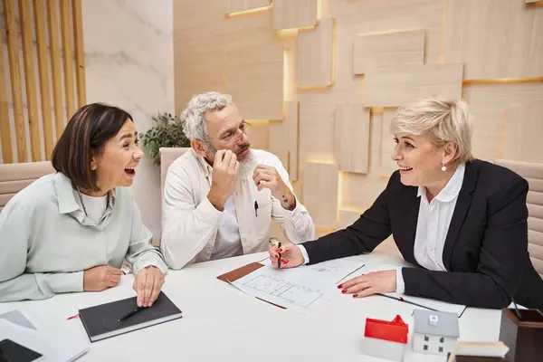 Cheerful middle aged married couple smiling near female realtor and discussing project of new house — Stock Photo