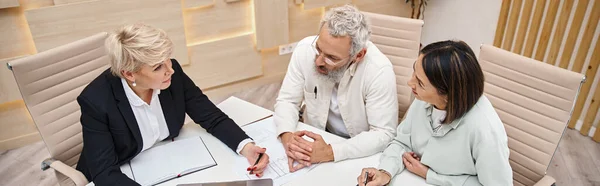 Middle aged female realtor discussing project of new house with married couple in office, banner — Stock Photo