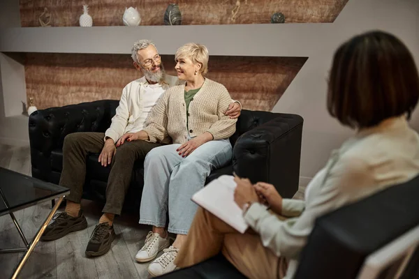 Bearded man hugging happy middle aged wife during therapy session with family counselor — Stock Photo