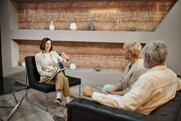 Positiver Psychologe gestikuliert, während er mit Ehepaaren mittleren Alters während einer Therapiesitzung spricht — Stockfoto
