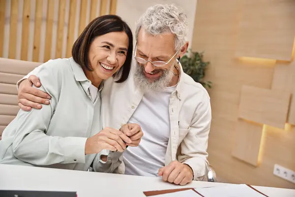 Щасливий бородатий чоловік обіймає багаторасову дружину тримає ключ від нового будинку в офісі нерухомості — стокове фото
