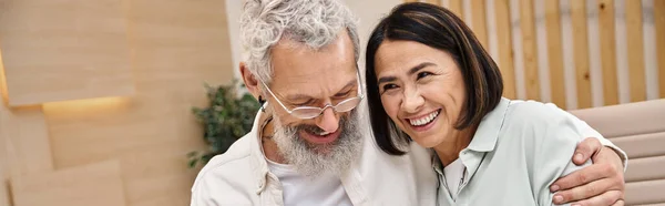 Hombre barbudo feliz abrazando a la esposa multirracial mientras compra una casa nueva en la oficina de bienes raíces, pancarta - foto de stock