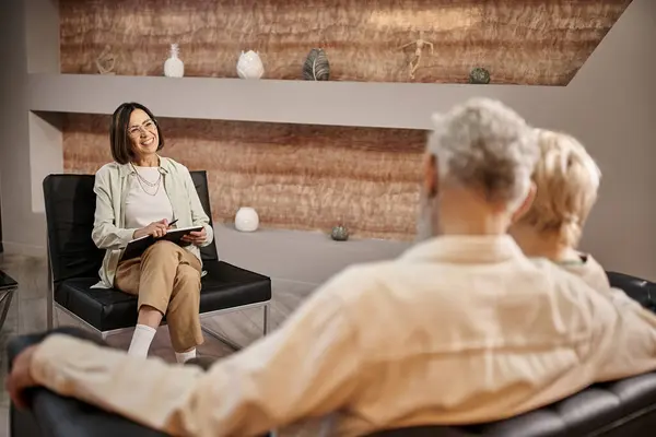 Middle aged psychologist in glasses sitting near married couple during family therapy session — Stock Photo