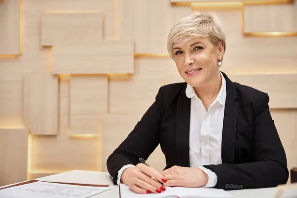 Happy blonde middle aged realtor with short hair working in real estate office, looking at camera — Stock Photo