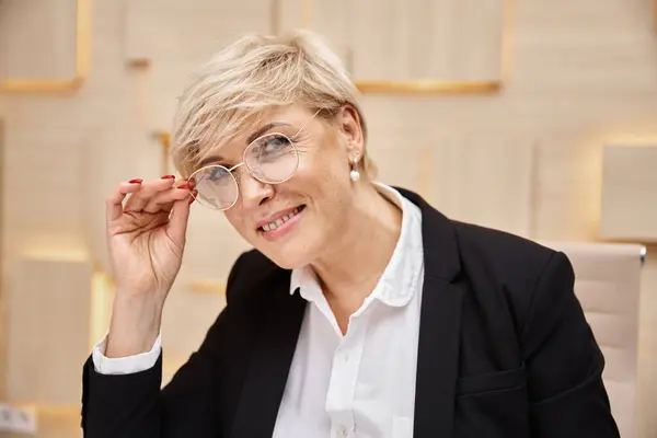 Щаслива блондинка середнього віку ріелтор в окулярах працює в офісі нерухомості, дивлячись на камеру — стокове фото
