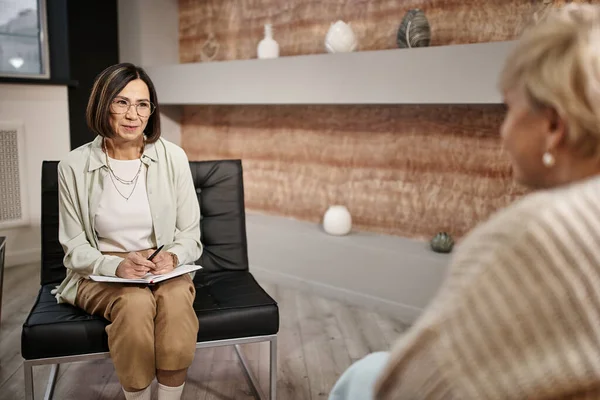 Psychologe mittleren Alters mit Brille lächelt und spricht mit blonder Frau während einer Therapiesitzung — Stockfoto