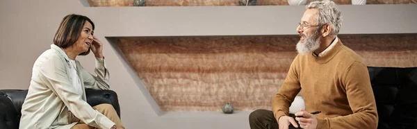 Бородатый психолог средних лет в очках разговаривает с клиенткой во время сеанса, баннер — стоковое фото