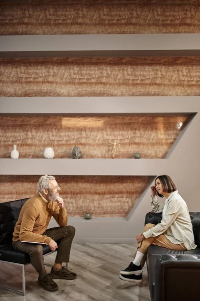 Bearded middle aged psychologist in glasses talking to female client during therapy session — Stock Photo