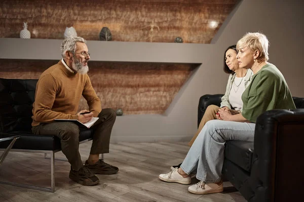Lesbian couple talking to bearded middle aged psychologist in glasses during therapy session — Stock Photo