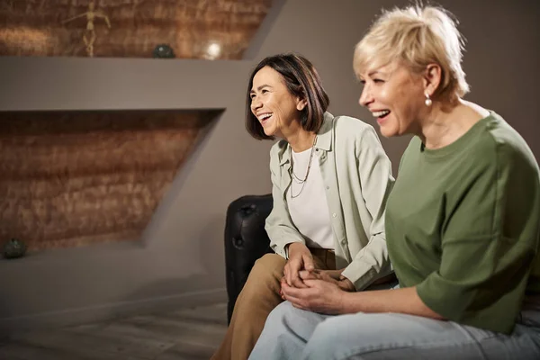 Cheerful  middle aged lesbian couple smiling while sitting on couch during therapy session — Stock Photo