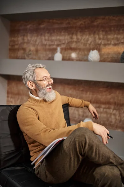 Glücklicher Psychologe mittleren Alters mit Brille, der während der Therapiesitzung lacht und auf einem Sessel sitzt — Stockfoto