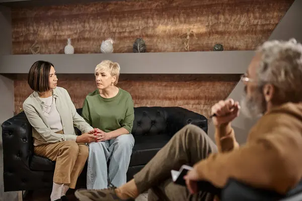 Psychologe mittleren Alters mit Brille hört besorgten lesbischen Paaren zu, die während der Sitzung sprechen — Stockfoto