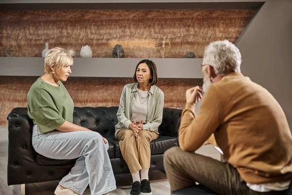 Lesbisches Ehepaar mittleren Alters spricht und sitzt während der Sitzung auf der Couch in der Nähe eines Psychologen — Stockfoto