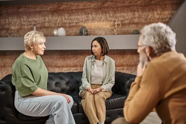 Middle aged married lesbian couple talking and sitting on couch near psychologist during session — Stock Photo