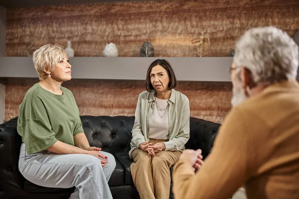 Lesbisches Ehepaar mittleren Alters spricht und sitzt während der Sitzung auf der Couch in der Nähe eines Psychologen — Stockfoto