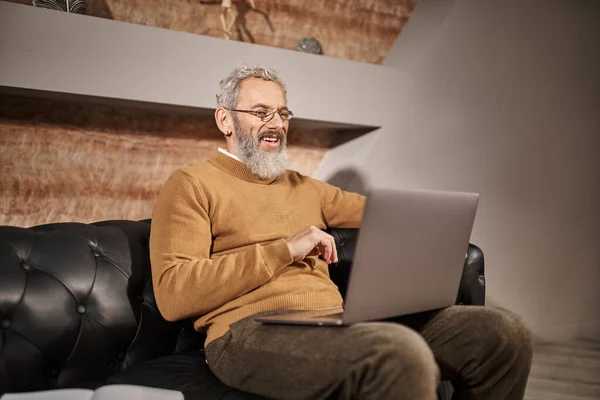 Psicólogo alegre de mediana edad con la barba hablando durante la consulta en línea con el cliente en el ordenador portátil - foto de stock
