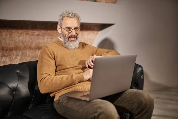 Веселый психолог средних лет со смехом бороды во время онлайн консультации с клиентом на ноутбуке — стоковое фото