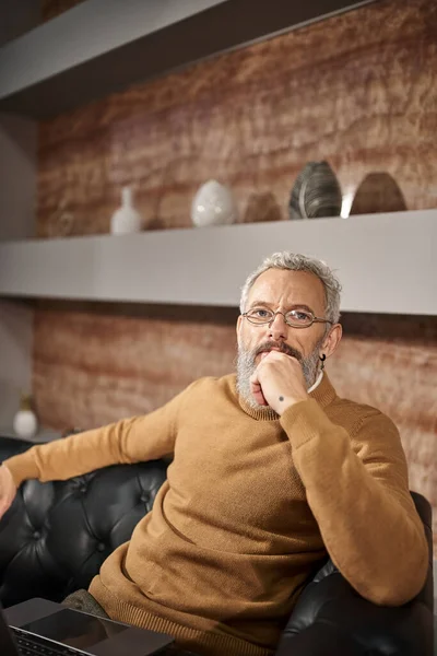 Psicologo di mezza età concentrato con barba seduta sul divano con laptop, consultazione online — Foto stock