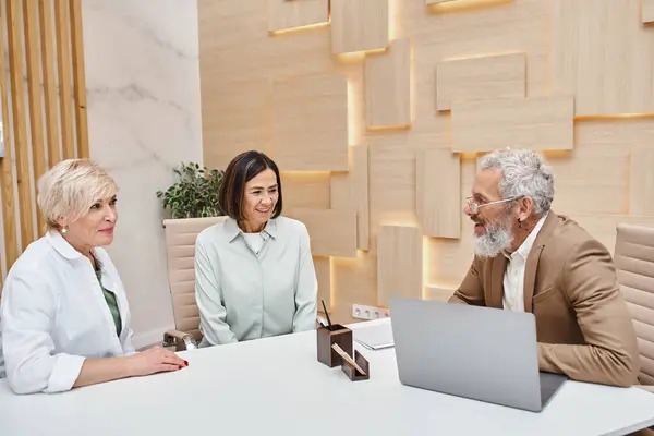 Smiling middle aged multicultural lgbt couple sitting next to bearded realtor in real estate office — Stock Photo