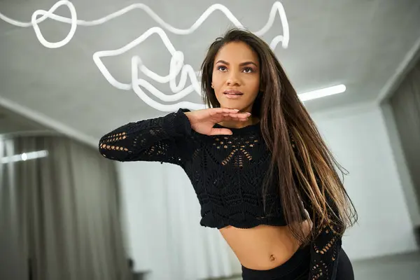Charming african american dancer in crop sweater touching long hair and looking away in studio — Stock Photo