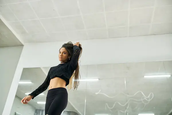 Atraente afro-americana de cabelos longos em traje preto ensaiando no estúdio de dança — Fotografia de Stock