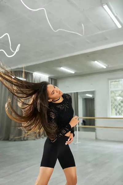 Long-haired artistic african american woman in black attire rehearsing rhythmic dance in modern hall — Stock Photo
