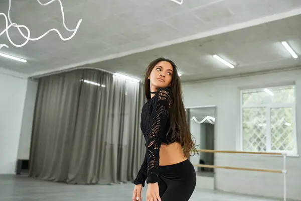 Professional long-haired african american dancer in black attire rehearsing in modern dance studio — Stock Photo