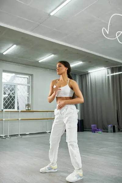 Stylish african american woman in white sports top and jogger pants dancing in studio, full length — Stock Photo