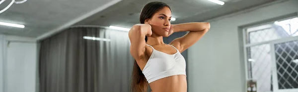 Trendy african american dancer in white sports top and pants adjusting long hair in studio, banner — Stock Photo