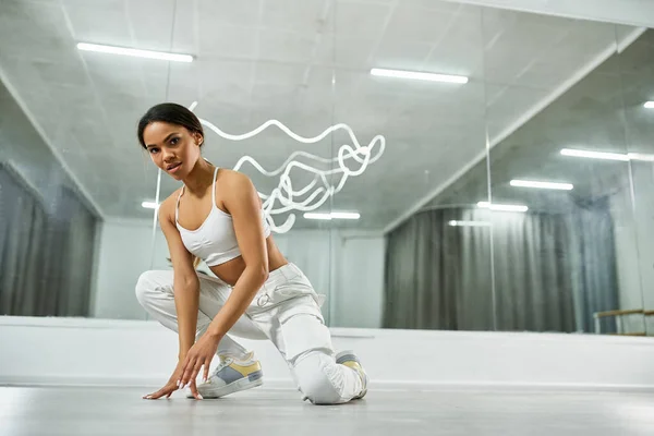 Trendy african american dancer in white sports top and pants looking at camera in  dance studio — Stock Photo