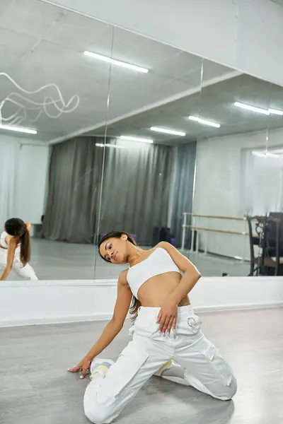 Dançarina afro-americana flexível em sportswear branco ensaiando no chão em estúdio, coreografia — Fotografia de Stock