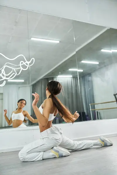 Artistic african american dancer in white sportswear exercising near mirror in studio, choreography — Stock Photo