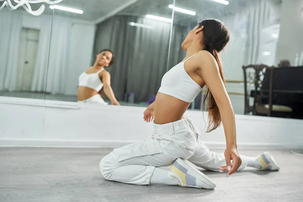 Профессиональная африканская американская танцовщица в белой спортивной одежде практикующая возле зеркала в студии, арктика — стоковое фото