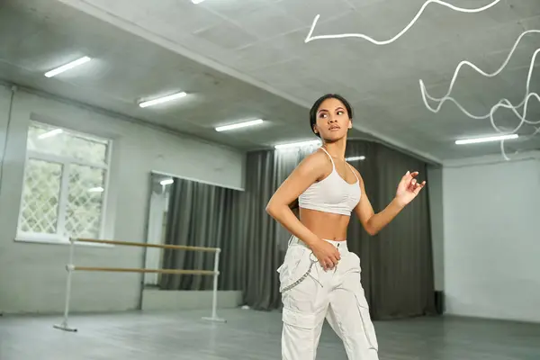 Dinâmico bailarino afro-americano em esportes brancos top ensaiando dança rítmica em estúdio espaçoso — Fotografia de Stock