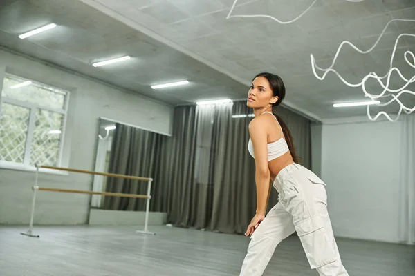 Graceful african american dancer in white sportswear rehearsing and training in modern studio — Stock Photo