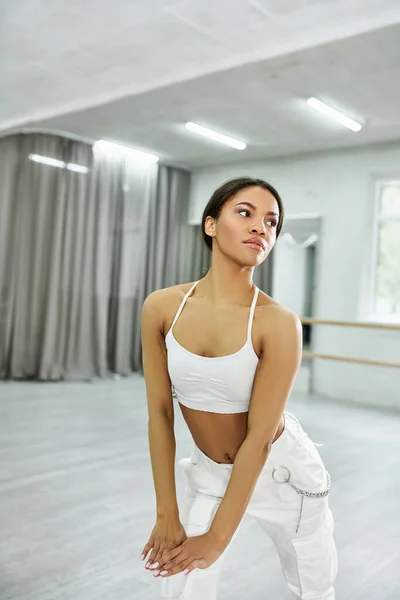 Graceful african american dancer in white sportswear rehearsing and training in modern dance hall — Stock Photo