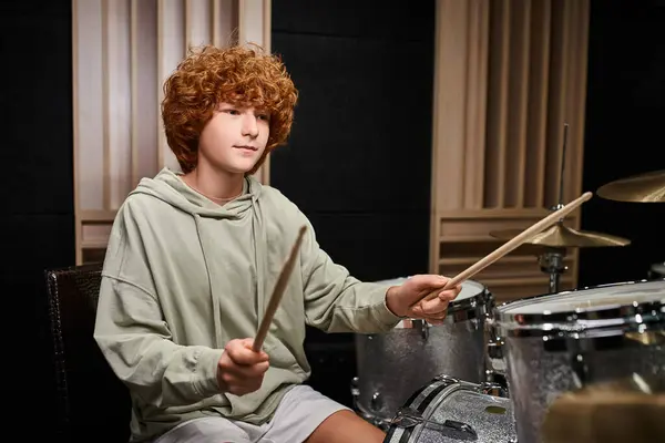Adorável focado adolescente com cabelo vermelho em traje aconchegante casual tocando sua bateria em estúdio — Fotografia de Stock